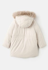 Svetlo béžová puffrová bunda s kapucňou lemovanou kožušinou, prešívanou textúrou a zúženým pásom. Má dlhé rukávy a ventilačný otvor na zadnej strane.