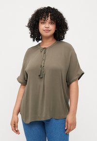Olive green short-sleeve blouse with a round neckline, decorative tie with tassels, and a relaxed fit. Smooth texture, lightweight fabric.