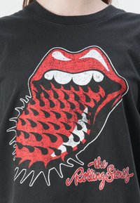 Black cotton t-shirt featuring a large red and white graphic of lips with jagged teeth and spikes, along with "the Rolling Stones" text.