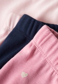 Opgestapelde, opgevouwen broeken in roze, marineblauw en lichtroze, met een klein wit hartdetail op de tailleband van de roze broek.