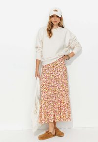Tenue décontractée composée d'un sweat-shirt crème, d'une jupe maxi à motifs floraux dans des teintes de rose et d'orange, et de chaussures marron à enfiler. Accessoirisée avec un tote blanc.