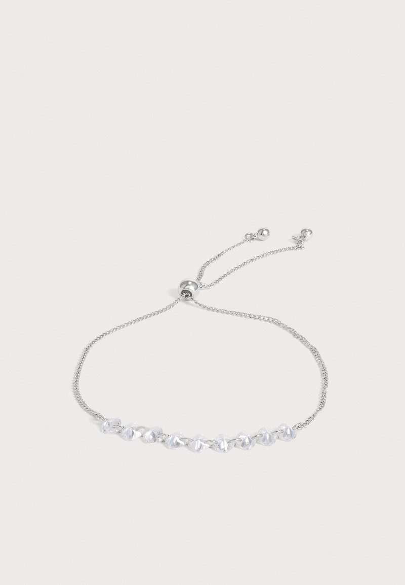 Bracelet délicat en argent réglable avec de petits cristaux clairs en forme de cube enfilés le long de la chaîne sur un fond clair uni.