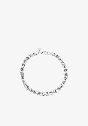 Bracelet en chaîne argentée avec des maillons rectangulaires entrelacés et une petite étiquette ronde près du fermoir, sur fond blanc.