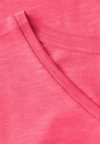 Pink bomuldsstof med en glat tekstur, prydet med et struktureret mønster og en rund halsudskæring med en forstærket søm.