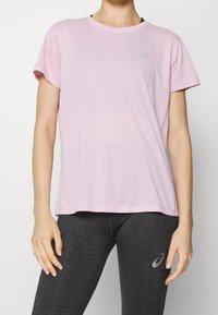 Camiseta deportiva de color rosa claro con cuello redondo y mangas cortas. Presenta una textura suave y un pequeño logo reflectante en el pecho.