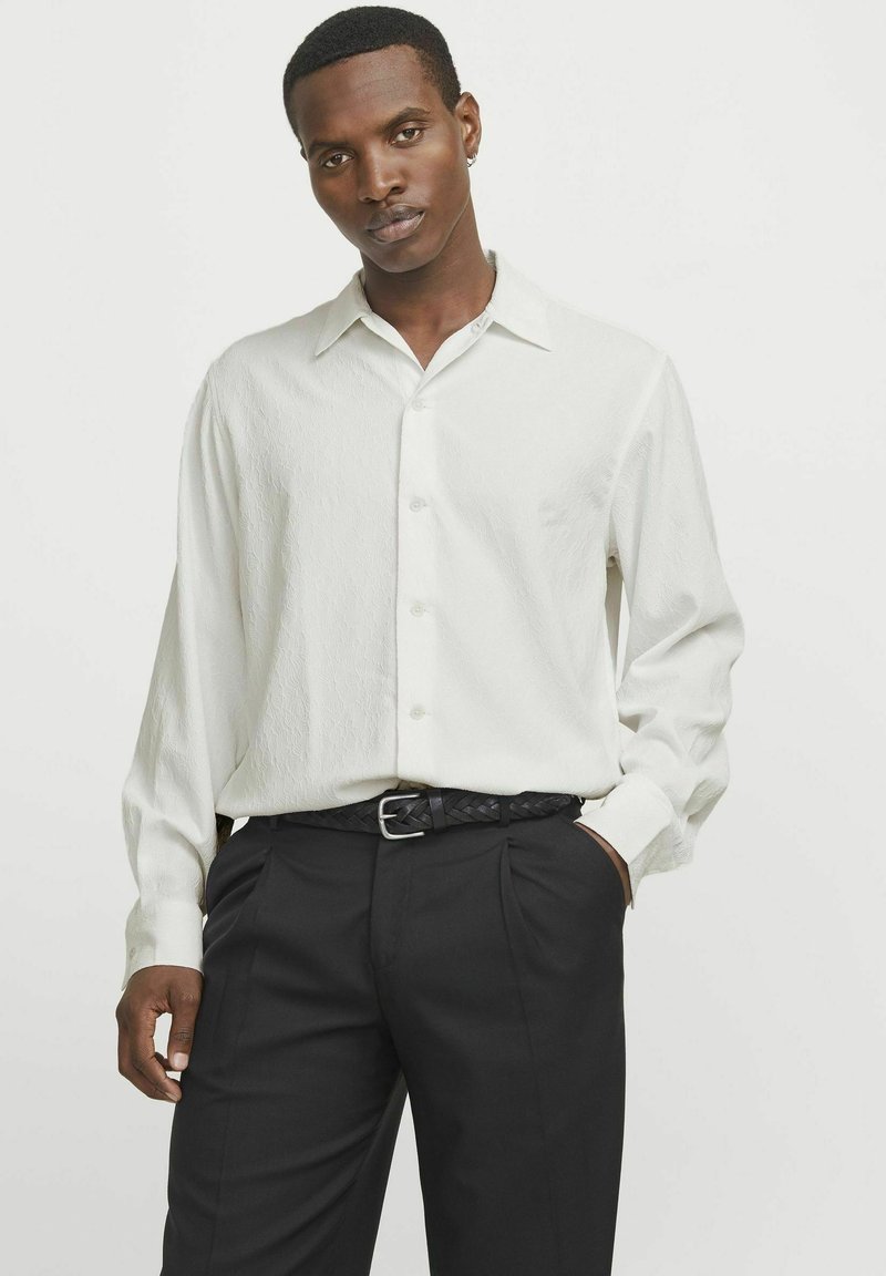 Witte, gestructureerde blouse met lange mouwen en een klassieke kraag, met knoopsluiting aan de voorkant, gecombineerd met zwarte geplooide broeken en een geweven zwarte riem.