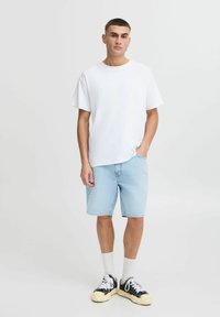 Camiseta blanca de algodón combinada con pantalones cortos de mezclilla azul claro, con un corte relajado, llevada con zapatillas negras y blancas y calcetines blancos.