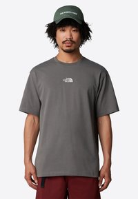 Šedé pánské tričko s krátkým rukávem, kulatým výstřihem a bílým logem na přední straně. Spárované se zelenou kšiltovkou s vyšitým textem.