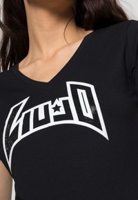 Czarny t-shirt z dekoltem w kształcie litery V z wyrazistym białym nadrukiem przedstawiającym gwiazdę i abstrakcyjne kształty. Wykonany z miękkiej bawełny o dopasowanym kroju.