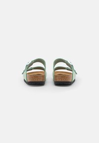 Green backless sandals with a cork footbed, adjustable straps, and a textured black outsole. Accents include a silver buckle.