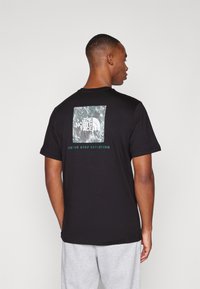 Camiseta de algodón negra con un gráfico cuadrado que presenta un diseño inspirado en la naturaleza y un logo, con el texto "NUNCA DEJES DE EXPLORAR" debajo.