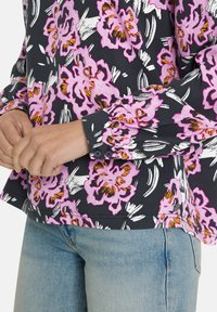 Black floral shirt featuring large pink flowers with orange accents, white leaves, and buttons on the cuffs; paired with light blue jeans.