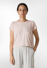 Ljusrosa bomullströja med korta ärmar och rundad halsringning, bärs tillsammans med ljusgrå löst sittande byxor. Enkel, odekorerad design.