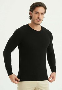 Pull en tricot noir avec des manches longues et un col rond. Le tissu présente une finition texturée, un ajustement près du corps et un ourlet côtelé.