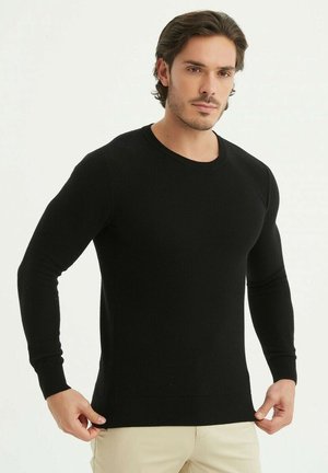 Pull en tricot noir avec des manches longues et un col rond. Le tissu présente une finition texturée, un ajustement près du corps et un ourlet côtelé.