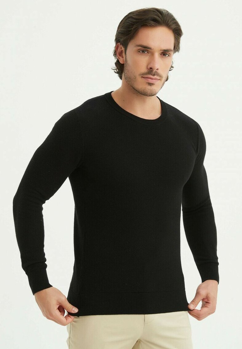Pull en tricot noir avec des manches longues et un col rond. Le tissu présente une finition texturée, un ajustement près du corps et un ourlet côtelé.