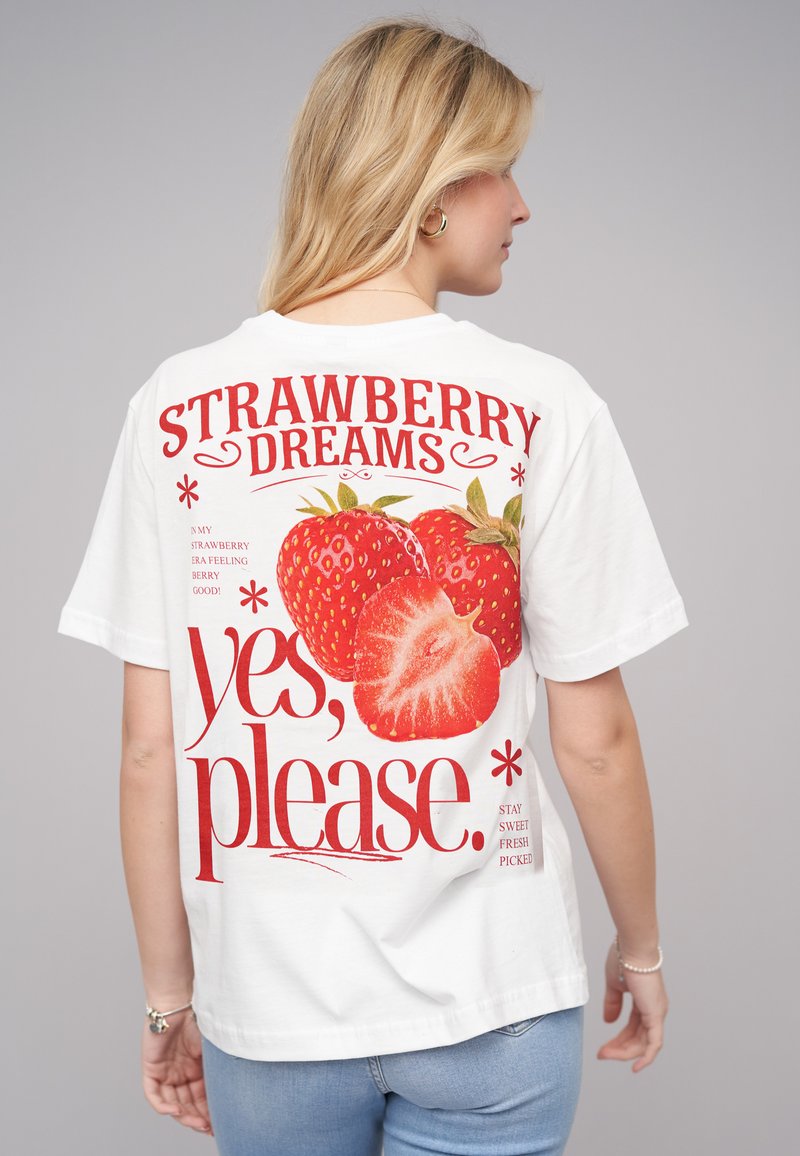 T-shirt en coton blanc avec un graphique de fraise rouge audacieux et le texte "RÊVES DE FRAISE oui, s'il vous plaît." Manches courtes, coupe décontractée.