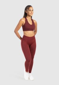 Completo sportivo in morbido tessuto elasticizzato composto da reggiseno color marrone e leggings. Presenta una scollatura a U, un ampio cinturino in vita e abbinato a scarpe da ginnastica bianche.