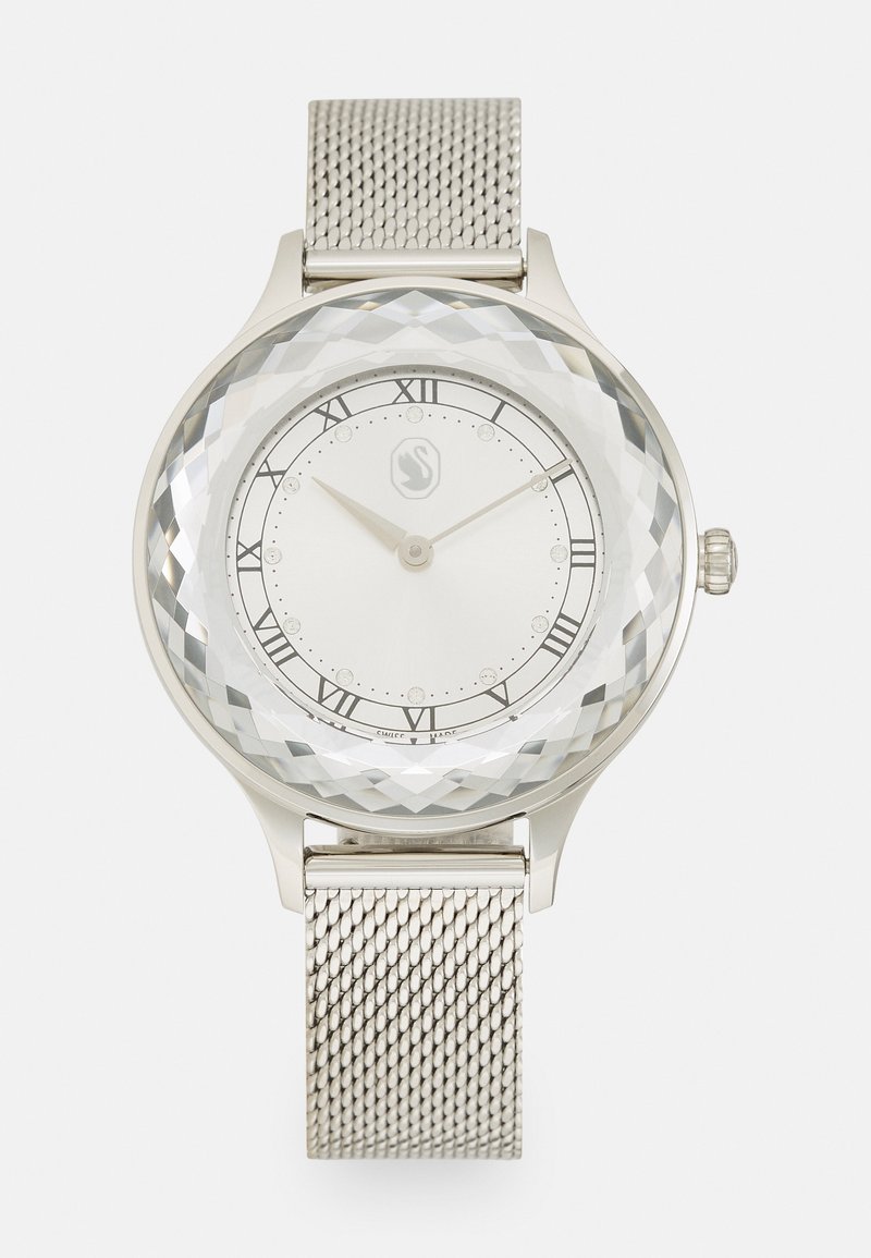 Silver mesh band watch with a faceted clear dial, white face, black Roman numerals, and small crystal accents.  Minimalist design.