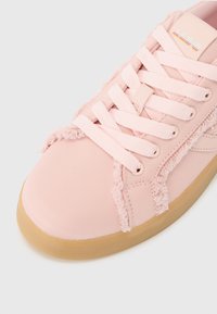 Pink canvas sneaker with textured, frayed edges, flat laces, and a gum rubber sole. Features a logo on the tongue.