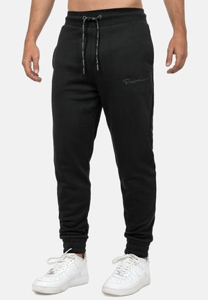 Black sweatpants made of soft fabric, featuring an elastic waistband with drawstring and ribbed cuffs. Embroidered logo detail on leg.