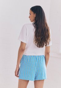 Camicia bianca a maniche corte abbinata a pantaloni corti a righe blu e bianche. I pantaloni corti presentano una vestibilità comoda e un tessuto testurizzato.