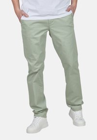 Pantalons en coton vert clair à coupe droite, dotés de deux poches avant et d'une texture lisse, associés à des baskets blanches.