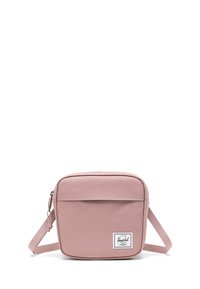 Čtvercová růžová crossbody taška vyrobená z odolné látky, obsahující přední kapsu, nastavitelné rameno a nášivku s logem v pravém dolním rohu.