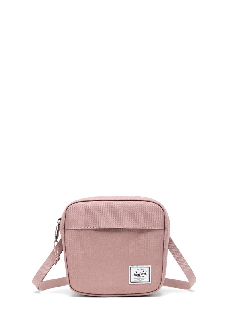 Čtvercová růžová crossbody taška vyrobená z odolné látky, obsahující přední kapsu, nastavitelné rameno a nášivku s logem v pravém dolním rohu.