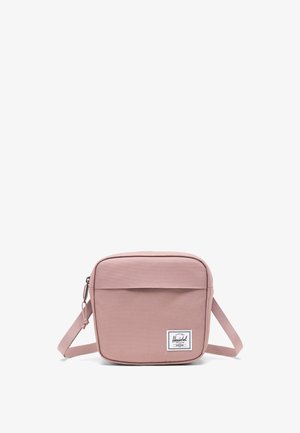 Čtvercová růžová crossbody taška vyrobená z odolné látky, obsahující přední kapsu, nastavitelné rameno a nášivku s logem v pravém dolním rohu.