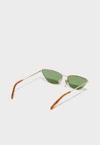 Ochelari de soare cu nuanță verde, cu o ramă subțire din metal aurit, lentile triungiulare și vârfuri ale templelor din acetat maro. Design minimalist și structură ușoară.