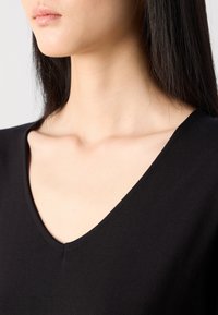 Black V-neck top made of smooth fabric; close-up view from the collarbone to chin, showcasing neckline and soft texture.