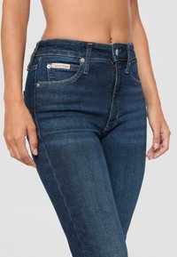 Tmavě modré džínové kalhoty s úzkým střihem, klasickým pětipocket designem, viditelným prošíváním a logem Calvin Klein na přední kapse.