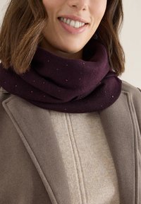 Écharpe en tricot bordeaux avec de petits pois roses et noirs, associée à un pull beige clair et un manteau gris avec des revers structurés.