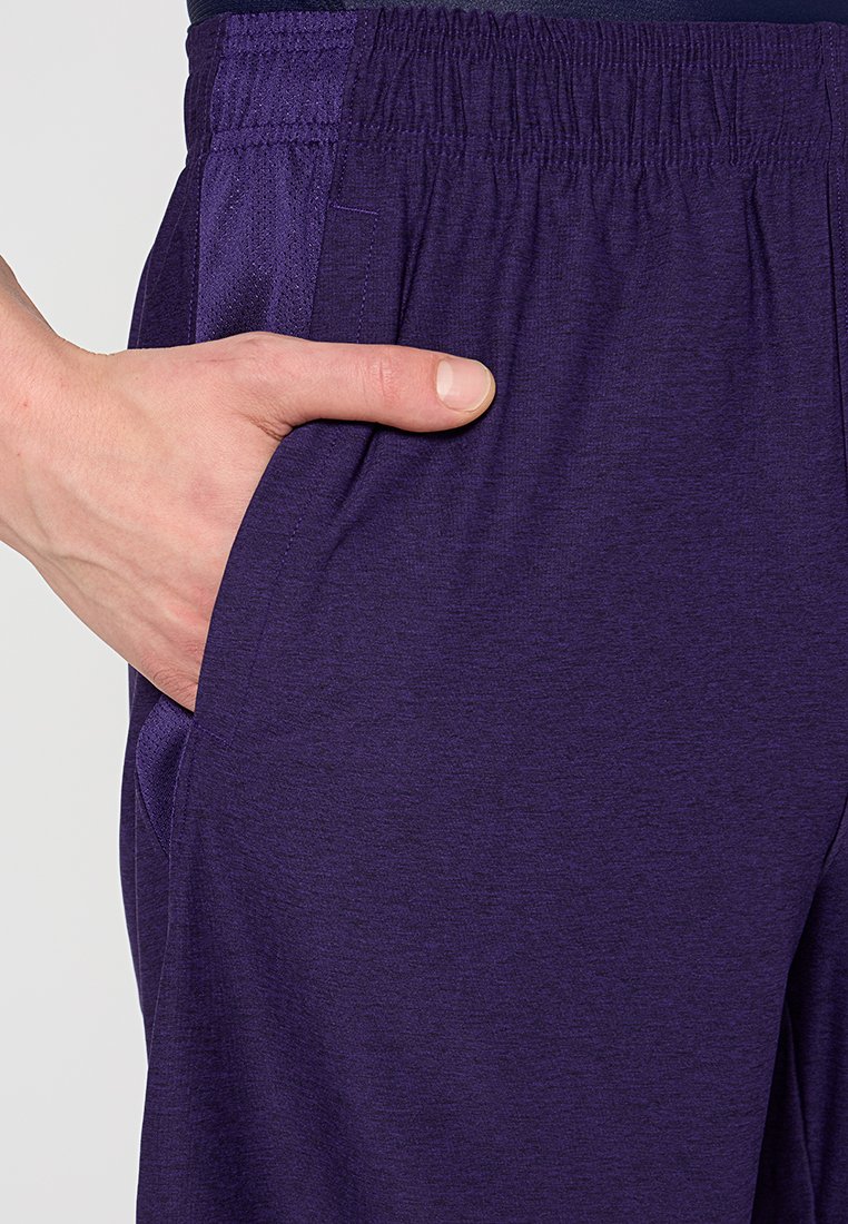Pantaloni sportivi viola con una texture liscia, vita elastica e tasche laterali. Presentano un dettaglio a pannello a contrasto lungo il lato.