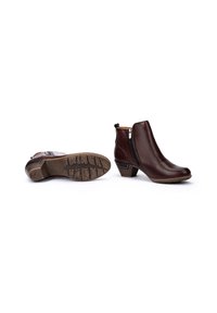 Par de botas de cuero marrón hasta el tobillo con cremallera lateral y tacón bajo apilado, una bota erguida y la otra de lado mostrando la suela.