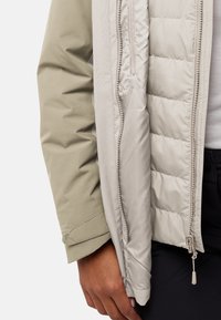 Gewatteerde jas met een lichtbeige binnenlaag en een zachte groene buitenlaag. Kenmerkt zich door een rits en stoffen accenten met een gladde textuur.