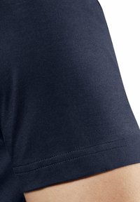 Granatowa koszula z krótkim rękawem, charakteryzująca się gładką fakturą i klasycznym krojem, z wyraźnymi szwami wzdłuż krawędzi dolnej i rękawów.