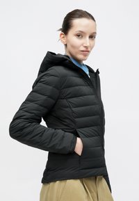 Fekete kapucnis steppelt dzseki cipzáros záródással és oldalzsebekkel. Kék galléros ing fölött viselve.