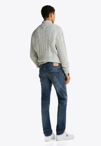 Jasnoszary sweter w splot warkoczowy z prążkowanym kołnierzem, zestawiony z ciemnoniebieskimi dżinsami i białymi trampkami z czerwonymi i niebieskimi akcentami.