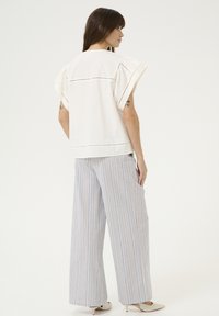 Top in cotone bianco con maniche corte e svasate, caratterizzato da un bordo in pizzo. Abbinato a pantaloni larghi a righe chiare e scarpe beige a punta.