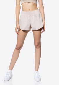 Shorts sportivi beige con una cintura elasticizzata, texture liscia e orlo curvo. Abbinati a sneaker bianche, con punta rotonda e lacci.