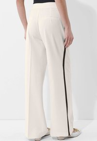 Witte wijde broek van gladde stof, met een zwarte zijstreep, achterzakken en een platte tailleband.