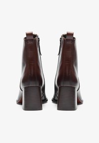 Brown leather ankle boots with a stacked heel, featuring a side zipper and clean stitching. Smooth texture with a minimalist design.