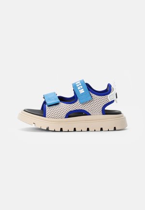 Sandálias leves com um upper em malha respirável bege e detalhes em azul, tiras ajustáveis em velcro e uma sola chunky bege.