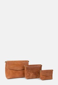 Three brown leather bags of varying sizes, featuring rounded shapes, flap closures, and smooth textures. No visible hardware or patterns.
