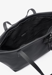 Sac fourre-tout en cuir noir avec fermeture éclair, intérieur spacieux, texture lisse et poignées plates. Comprend un petit accent détachable.