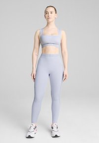 Ljusgrå sport-bh och matchande högmidjade leggings tillverkade av stretchigt material. Accentuerade med en märkesresår och sidodetaljer.