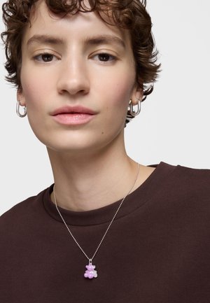 Collana in argento con ciondolo a forma di orso in rosa e bianco. Lo sfondo è neutro e il modello indossa una maglietta marrone scuro.