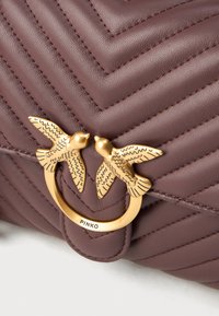 Dark burgundy leather bag with chevron quilted pattern, featuring a gold-tone double-bird hardware clasp and embossed logo.